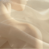 Delikatne, minimalistyczne, abstrakcyjne zdjęcie. Zbliżenie delikatnej, półprzezroczystej tkaniny, delikatnie się układającej i płynącej, symbolizującej powięź. Naturalne, ciepłe światło, subtelne cienie, kremowe odcienie beżu. Uczucie rozluźnienia, miękkości, powolnego ruchu. W tle obraz kobiety, jako symbol delikatności.