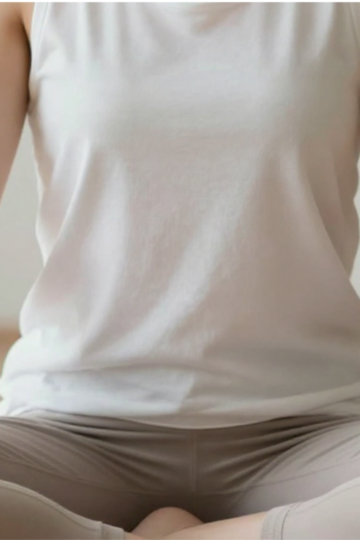 Minimalistyczne zdjęcie przedstawiające osobę siedzącą w skupieniu, z dłońmi opartymi na udach, rozluźnionymi ramionami i neutralną postawą. Nacisk położony na spokój, uziemienie i regulację układu nerwowego. Łagodne światło dzienne, naturalne tony, delikatne cienie. Terapeutyczne, pełne świadomości ciała, spokoju somatycznego. Bez szczegółów medycznych i anatomicznych.